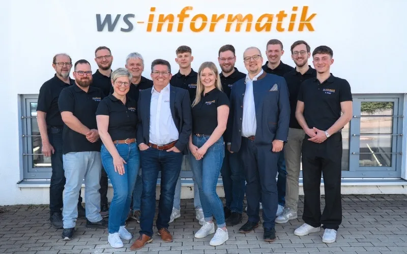 Gruppenfoto des Teams der WS-Informatik GmbH & Co. KG vor dem Firmengebäude. Obere Reihe von links: Walter, Michael, Volker, Benedikt, Alexander, Marvin, Luis. Untere Reihe von links: Sven, Sandra, Dr. Stephan Werner, Lea, Jan Steinhadt, Elias.