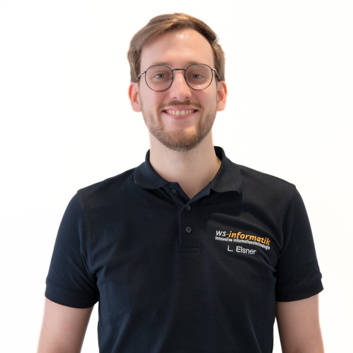 Portrait von Luis, Softwareentwickler bei der WS-Informatik GmbH & Co. KG, im schwarzen Poloshirt mit Firmenlogo, vor weißem Hintergrund.
