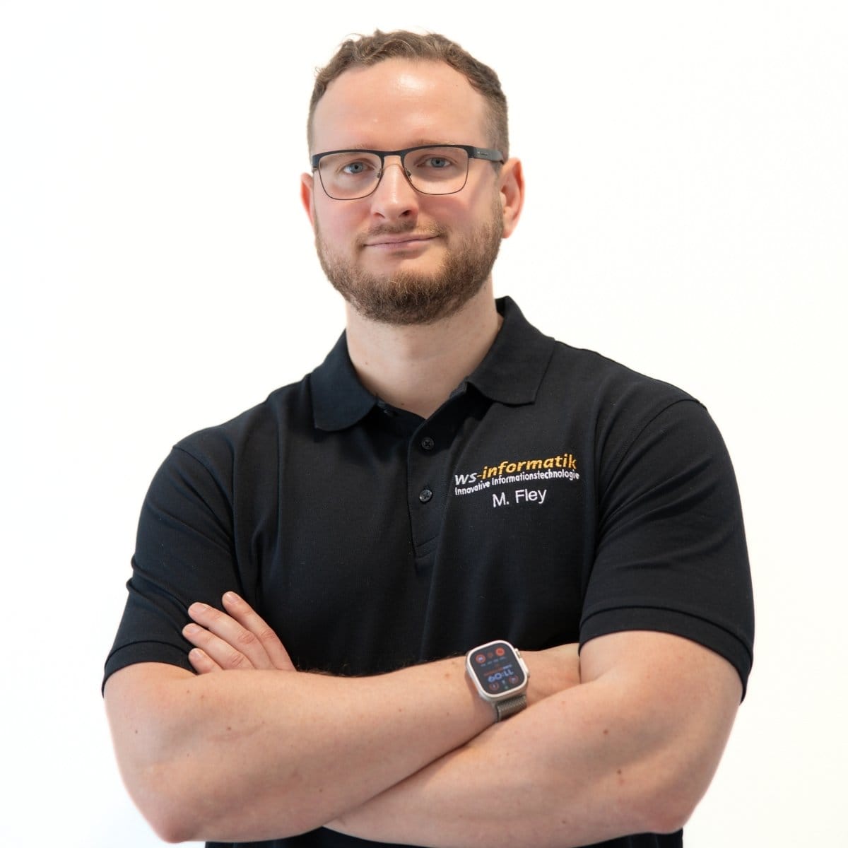 Portrait von Michael, Servicetechniker bei der WS-Informatik GmbH & Co. KG, im schwarzen Poloshirt mit Firmenlogo, vor weißem Hintergrund, mit verschränkten Armen.