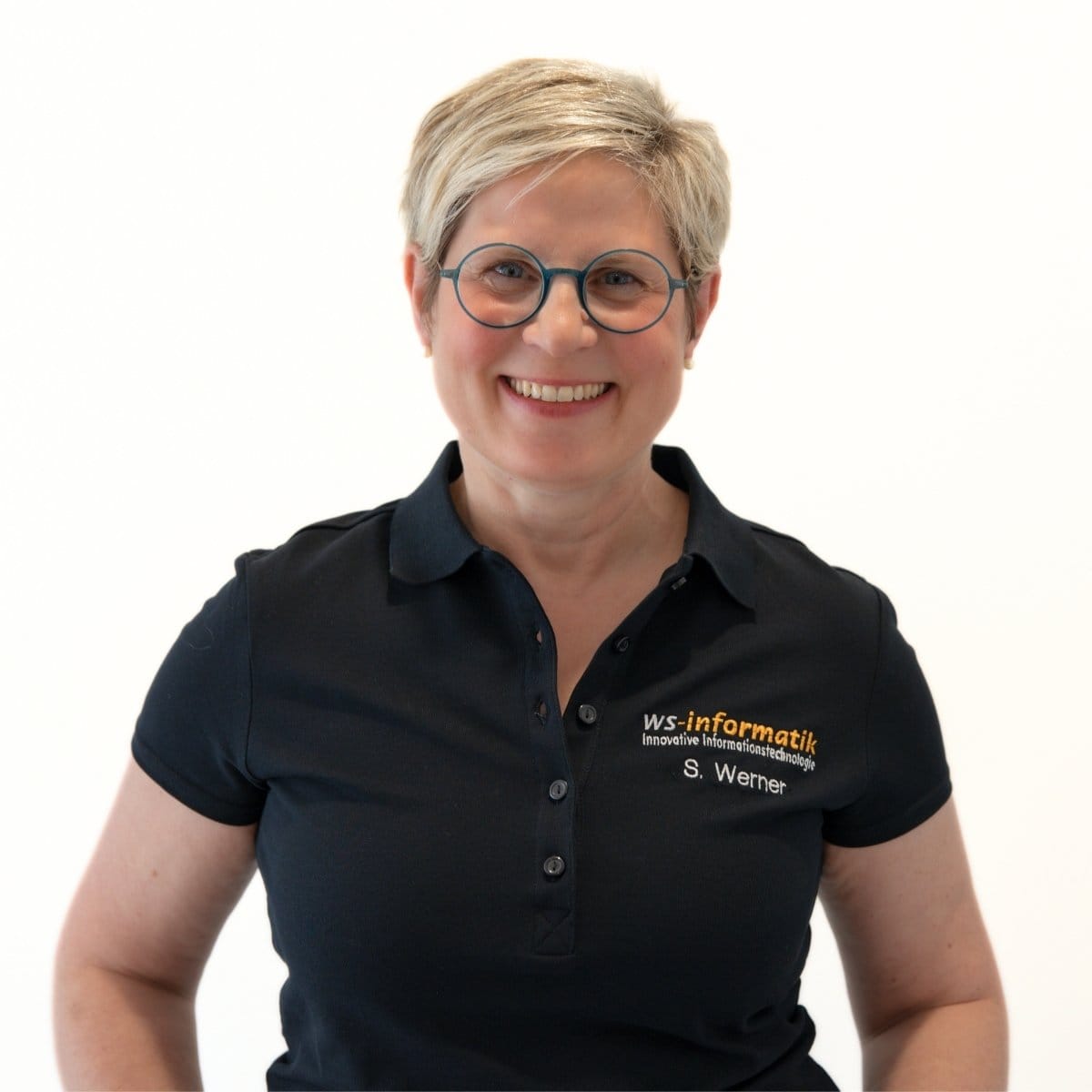 Portrait von Sandra, Mitarbeiterin bei der WS-Informatik GmbH & Co. KG, im schwarzen Poloshirt mit Firmenlogo, vor weißem Hintergrund.