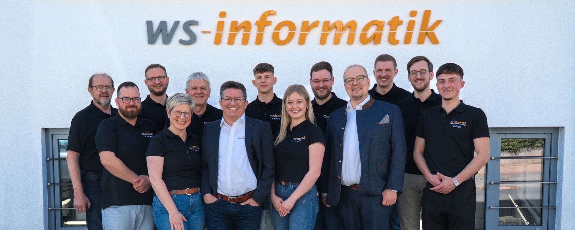 Gruppenfoto des Teams der WS-Informatik GmbH & Co. KG vor dem Firmengebäude. Obere Reihe von links: Walter, Michael, Volker, Benedikt, Alexander, Marvin, Luis. Untere Reihe von links: Sven, Sandra, Dr. Stephan Werner, Lea, Jan Steinhadt, Elias.